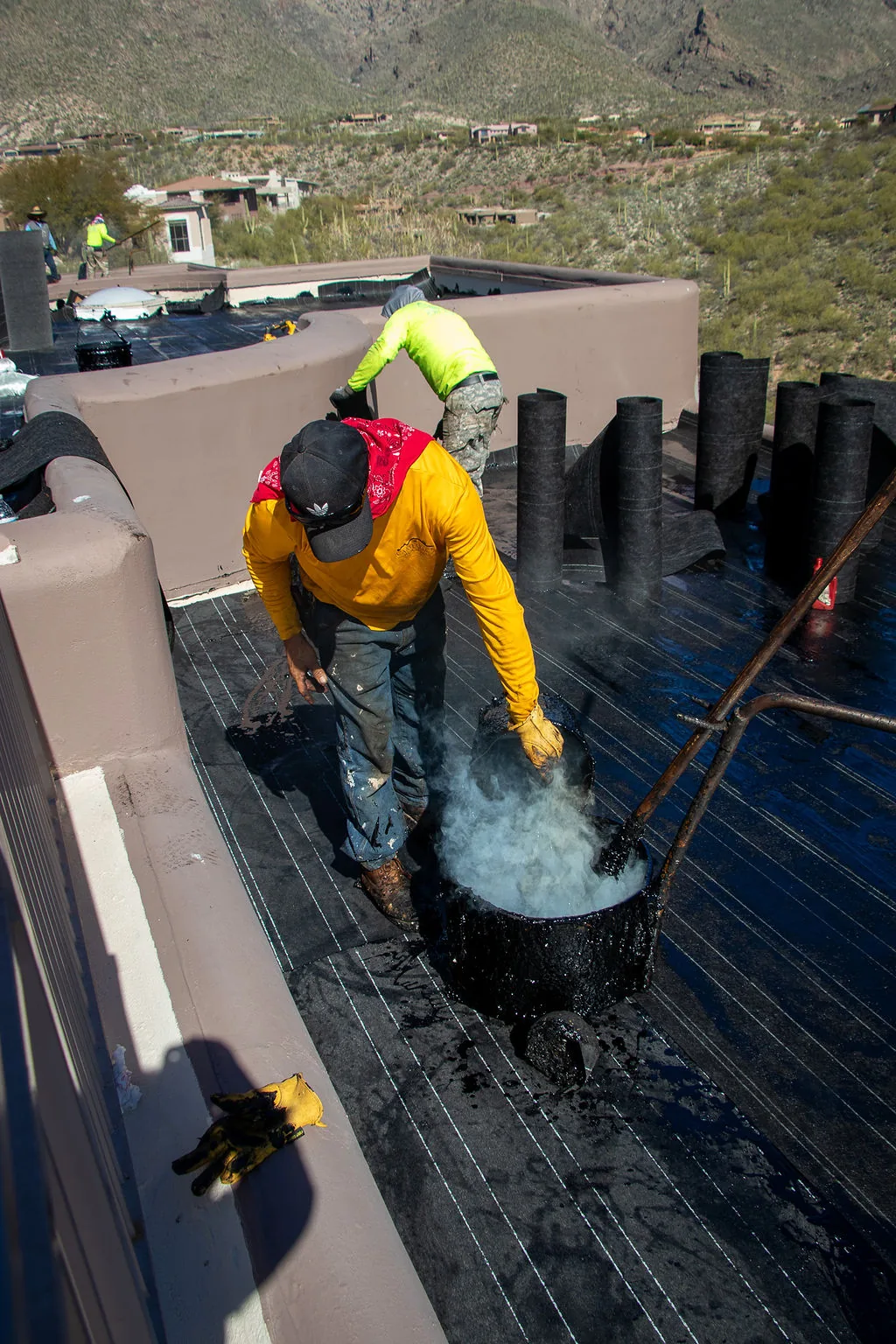 Roofer stirring a bucket of hot tar on a flat roof